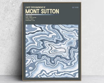 May include: A framed topographic map print of Mont Sutton, Quebec, featuring a dark gray background with cream text and a blue and white contour line pattern. The text reads: CARTE TOPOGRAPHIQUE DE MONT SUTTON, QC-008, ESTRIE, QUÉBEC, MASSIF: MONTS SUTTON, ALTITUDE: 968 M, ÉQUIDISTANCE: 20 M.