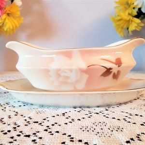Puede incluir: Una salsera de porcelana blanca con un diseño floral rosa y dorado. La salsera tiene un platillo a juego.