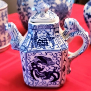 Puede incluir: Una tetera de porcelana azul y blanca con un asa de dragón y tapa. La tetera tiene un diseño floral y un patrón geométrico.
