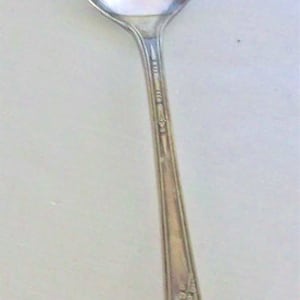 May include: A silver spoon with an ornate design on the handle. The spoon is polished and shiny.