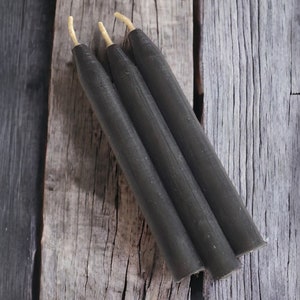 May include: Three black taper candles with natural wicks on a wooden surface.