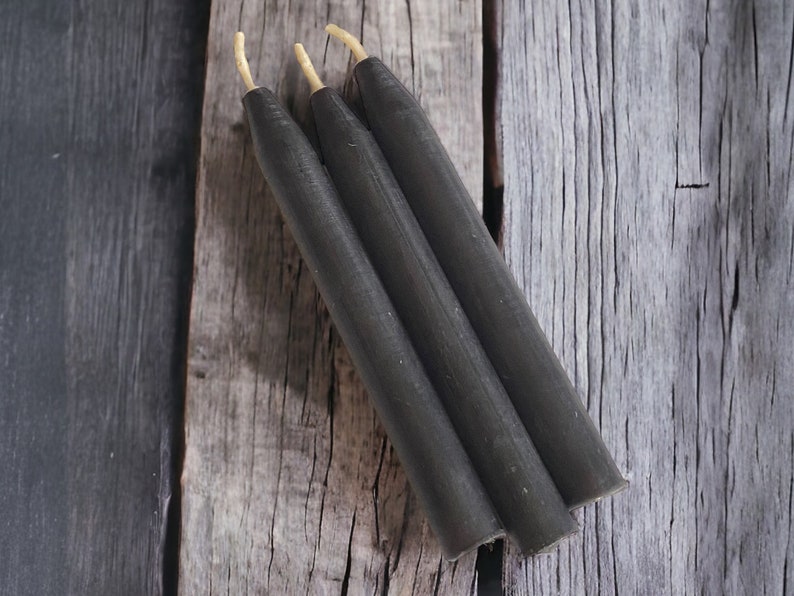 May include: Three black taper candles with natural wicks on a wooden surface.