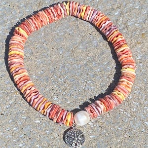 May include: A colorful bracelet made of small, flat, shell pieces in shades of orange, yellow, and purple. A white pearl and a silver sand dollar charm dangle from the bracelet.