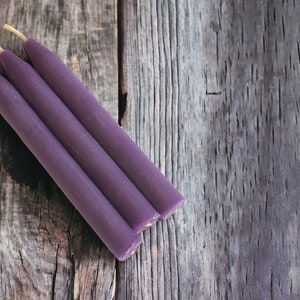 May include: Three purple chime candles with a natural wick on a weathered wooden surface.