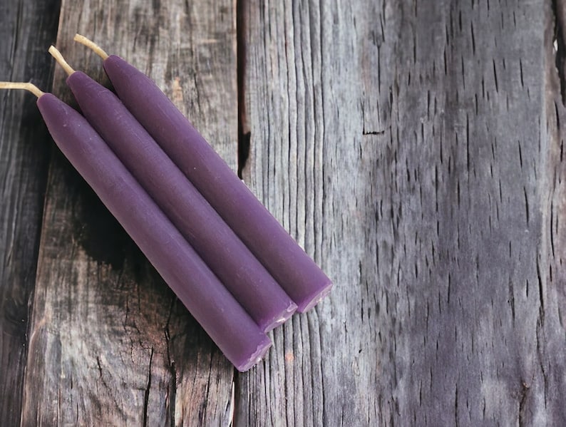 May include: Three purple chime candles with a natural wick on a weathered wooden surface.