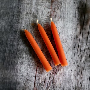 May include: Three orange  candles on a weathered wood surface.
