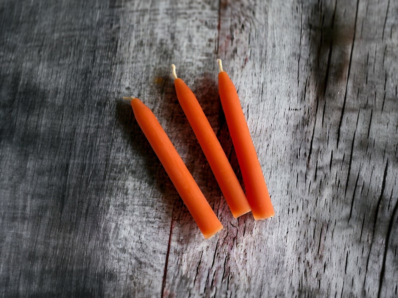 May include: Three orange  candles on a weathered wood surface.