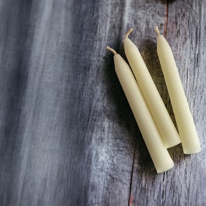May include: Three white  candles on a gray wooden surface.