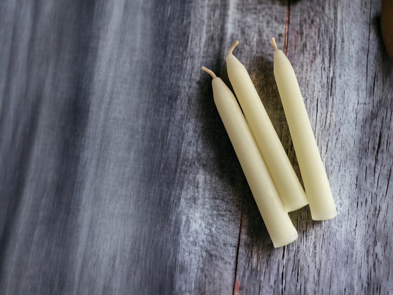 May include: Three white  candles on a gray wooden surface.