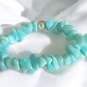 May include: A turquoise chip bead bracelet with a gold-colored bead accent. The bracelet is made of small, irregular-shaped beads in varying shades of blue-green. The beads are strung together to form a circular shape.