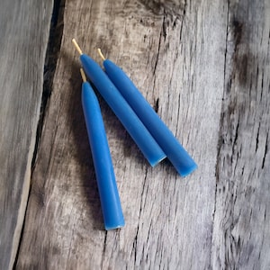 May include: Three blue candles with natural wicks on a wooden surface.