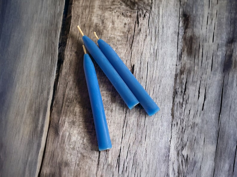 May include: Three blue candles with natural wicks on a wooden surface.