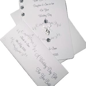 May include: A white wedding card set with silver script and embellishments. The main card reads "With Love To Our Daughter & Son-in-law On Your Wedding Day." A smaller card says "A Wedding Day Gift For You Both."