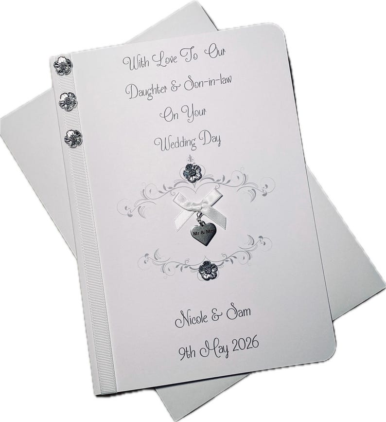 May include: A white wedding card with the text "With Love To Our Daughter & Son-in-law On Your Wedding Day". The card features decorative embellishments, a ribbon, and the names "Nicole & Sam" with the date "9th May 2026".