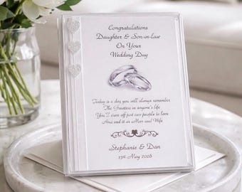 May include: A white wedding card with the text "Congratulations Daughter & Son-in-law On Your Wedding Day". The card features a pair of wedding rings and is decorated with three heart-shaped embellishments. The names "Stephanie & Dan" and the date "15th May 2028" are also printed on the card.