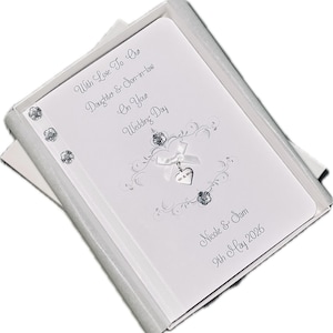 May include: A white wedding card with silver text and embellishments, presented in a white box. The card reads "With Love To Our Daughter & Son-in-law On Your Wedding Day" and includes the names "Nicole & Sam" and the date "9th May 2026".