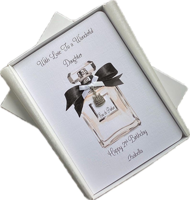 May include: A white greeting card with a perfume bottle illustration, black bow, and silver charm, inside a white box. Text reads "With Love To a Wonderful Daughter", "Happy 21st Birthday", and "Isabella".