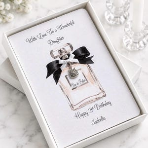 May include: A white rectangular greeting card in a box featuring a watercolor illustration of a perfume bottle with a black and white ribbon and a silver cake charm. The text reads: With Love To a Wonderful Daughter, Eau de Parfum, Happy 21st Birthday, Isabella.