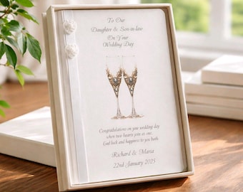 May include: A wedding card in a white box. The card reads "To Our Daughter & Son-in-law On Your Wedding Day." It features two champagne glasses and the names Richard & Maria, with the date January 22nd, 2025.