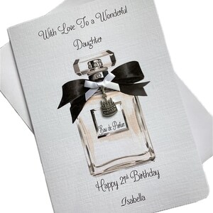 May include: A birthday card with a perfume bottle design. The card features the text "With Love To a Wonderful Daughter", "Happy 21st Birthday", and the name "Isabella". The perfume bottle has a black bow and a charm that says "Happy Birthday".