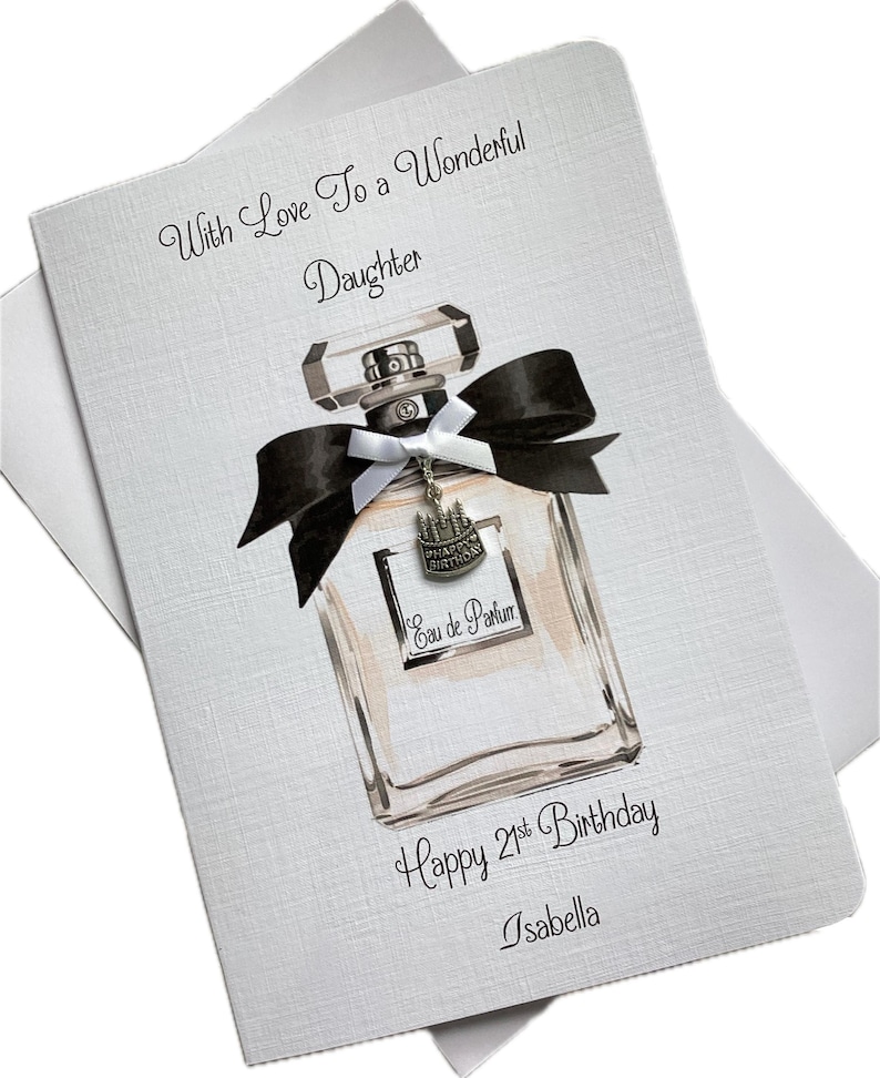 May include: A birthday card with a perfume bottle design. The card features the text "With Love To a Wonderful Daughter", "Happy 21st Birthday", and the name "Isabella". The perfume bottle has a black bow and a charm that says "Happy Birthday".