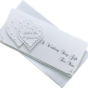 May include: White wedding day gift card with two heart-shaped embellishments. The card reads "Joshua & Mia 26th January 2025" and "A Wedding Day Gift For You". The card has a decorative edge and is placed on top of a white envelope.