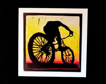 Può includere: Una stampa a linoleum in bianco e nero di una persona che guida una bicicletta su uno sfondo di tramonto giallo, arancione e rosso.