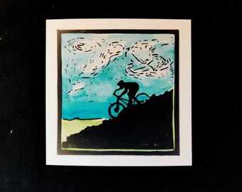 Può includere: Una stampa a linoleum in bianco e nero di una persona che guida una mountain bike in salita. Lo sfondo è un cielo blu con nuvole bianche.
