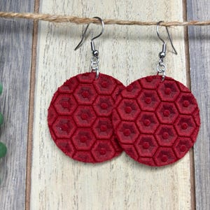 May include: A pair of red leather earrings with a hexagonal pattern. The earrings are hanging from silver hooks.