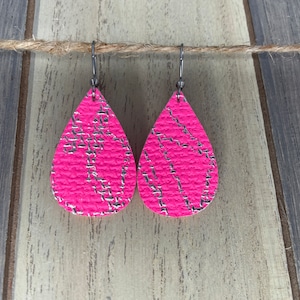May include: A pair of pink teardrop-shaped earrings with silver glitter accents. The earrings have silver hooks.