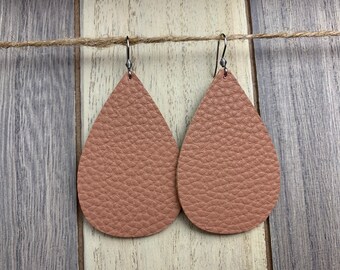 Peut inclure: Une paire de boucles d'oreilles en cuir en forme de goutte d'eau de couleur brun clair. Les boucles d'oreilles ont une surface texturée et sont suspendues à des crochets argentés.