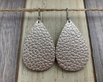 May include: A pair of silver teardrop-shaped earrings with a textured leather finish. The earrings are hanging from silver hooks.