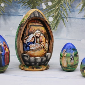 Peut inclure: Un ensemble de quatre œufs en bois peints à la main représentant la scène de la Nativité. Le plus grand œuf est ouvert pour révéler une scène détaillée de Marie, Joseph et l'enfant Jésus dans une crèche. Les trois autres œufs représentent les trois mages, un berger et une étable.
