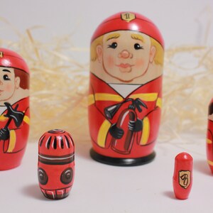 May include: Set of five red and yellow painted wooden nesting dolls, or matryoshka dolls, depicting firefighters. The largest doll is holding a red fire extinguisher, the second largest doll is holding an axe, the third largest doll is holding a fire hose, the fourth largest doll is holding a fire hydrant, and the smallest doll is holding a fire alarm.