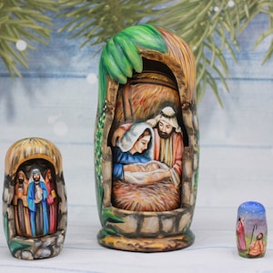 May include: A set of three wooden nesting dolls depicting the Nativity scene. The largest doll shows Mary, Joseph, and baby Jesus in a manger. The middle doll shows three wise men, and the smallest doll shows a shepherd with a sheep.