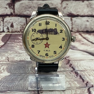 May include: A vintage silver wristwatch with a white face and black leather strap. The watch face features a red star and the text "С.Ж.Д. СССР". A black and white image of a train is in the background.