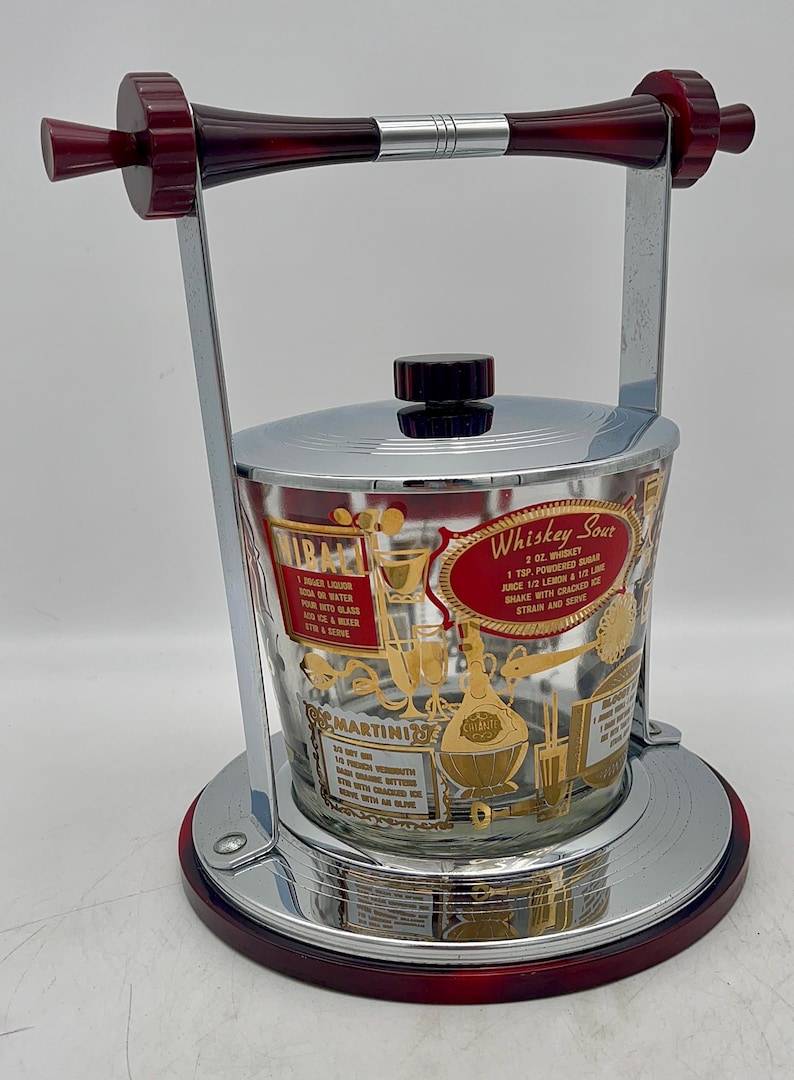 May include: Vintage cocktail ice bucket with a chrome and red handle and base. The clear glass bucket has gold lettering and illustrations for cocktail recipes, including "Whiskey Sour" and "Martini".