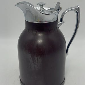 Könnte beinhalten: Eine vintage braune und silberne Thermoskanne mit einem verchromten Deckel und Griff.