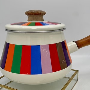Könnte beinhalten: Ein weißer Emaille-Topf mit einem Holzgriff und Deckel. Der Topf hat ein buntes Streifenmuster in den Farben Orange, Rot, Grün, Blau, Lila und Braun.