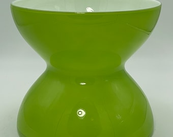 May include: A green glass bowl with a white interior. The bowl has a wide, round top and a narrow middle section, giving it a unique hourglass shape.