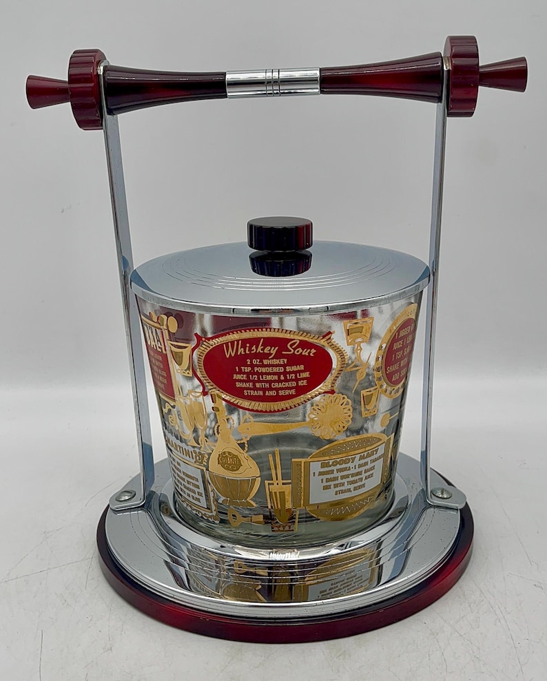May include: Vintage chrome and glass ice bucket with a red handle and base. The glass bucket features gold lettering and illustrations, including a recipe for a "Whiskey Sour" cocktail. The bucket is approximately 7 inches tall.