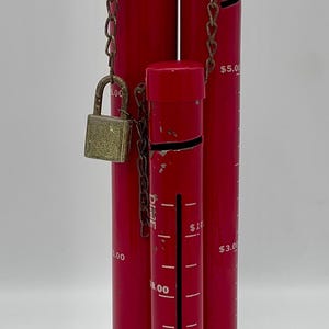 May include: A red metal coin bank with three separate compartments. Each compartment has a slot for coins and a scale to track the amount of money saved. The largest compartment has a lock and chain.
