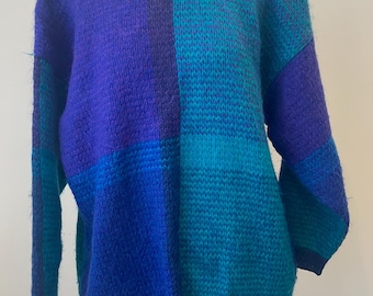 May include: A blue and teal color block sweater with a fuzzy texture. The sweater has a crew neck and long sleeves.