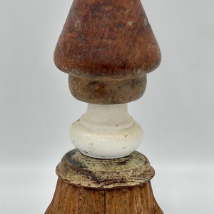 May include: A wooden finial with a brown, white and green paint finish. The finial has a pointed top and a fluted base.