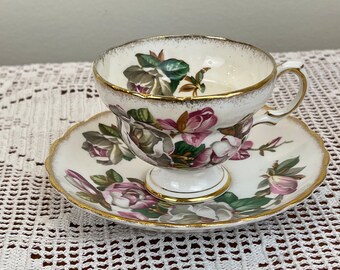 May include: A white teacup and saucer with a gold rim and floral pattern. The flowers are pink, white, and green.