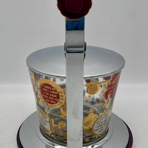 May include: Vintage cocktail shaker with a red and chrome finish. The glass cup features gold and red graphics with text. The shaker has a red handle and a chrome lever. The base is red and chrome.