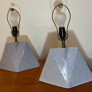 Può includere: Due lampade da tavolo in ceramica grigia con basi geometriche e dettagli in ottone. Le lampade hanno lampadine bianche.