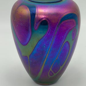Puede incluir: Un pequeño jarrón de vidrio iridiscente con un patrón de espiral azul, morado y verde.