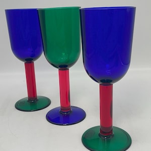 Puede incluir: Tres copas de vino coloridas con un diseño moderno. Los cuencos son azules o verdes, los tallos son rojos y las bases son verdes o azules. Las copas están dispuestas en fila sobre un fondo blanco.