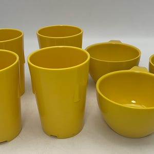 May include: Set of seven yellow ceramic cups and bowls. The cups are tall and cylindrical, while the bowls are round and shallow.